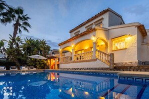 Une villa de luxe dotée d’une piscine, présentant un style architectural méditerranéen avec des arches et un toit en tuiles.