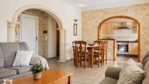 A living room with a sofa, a dining table with chairs, and a kitchen area with cabinets and a stove.