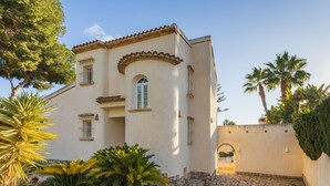 A two-story building with a stone-paved entrance, surrounded by tropical plants and palm trees.