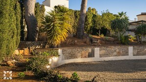 A landscaped area with a stone wall, trees, and a white building.