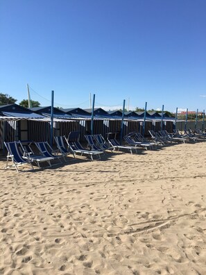 A beach with rows of numbered beach huts and lounge chairs.