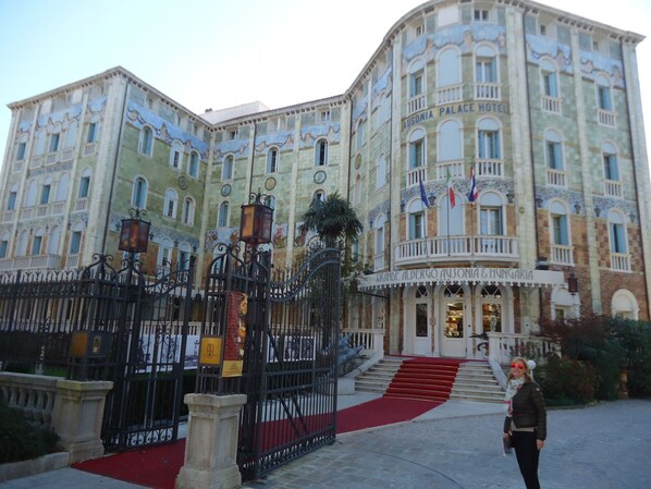 A large, historic building with a grand entrance, multiple balconies, and a red carpet leading to the entrance.