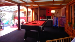 Une table de billard dans une pièce avec des poutres en bois et un plafond en verre, un canapé et une petite table avec des chaises.