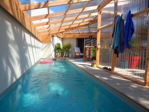 An indoor swimming pool with a wooden ceiling and glass walls, surrounded by potted plants and a seating area. - seaside villa with pool (plounéour-trez)