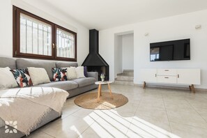 A modern living room with a sofa, a fireplace, a TV, and a staircase.