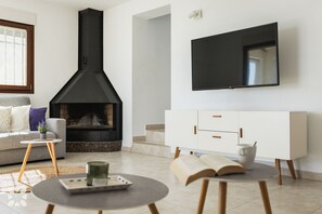 A living room with a fireplace, a sofa, a coffee table, a TV mounted on the wall, and a white cabinet.
