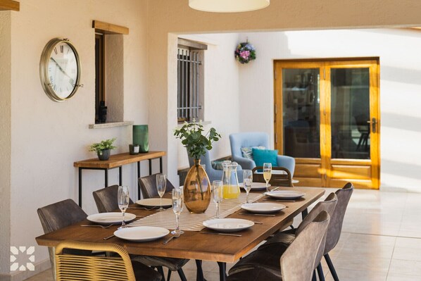 A dining area with a wooden table set for four, a vase with flowers, and a clock on the wall.