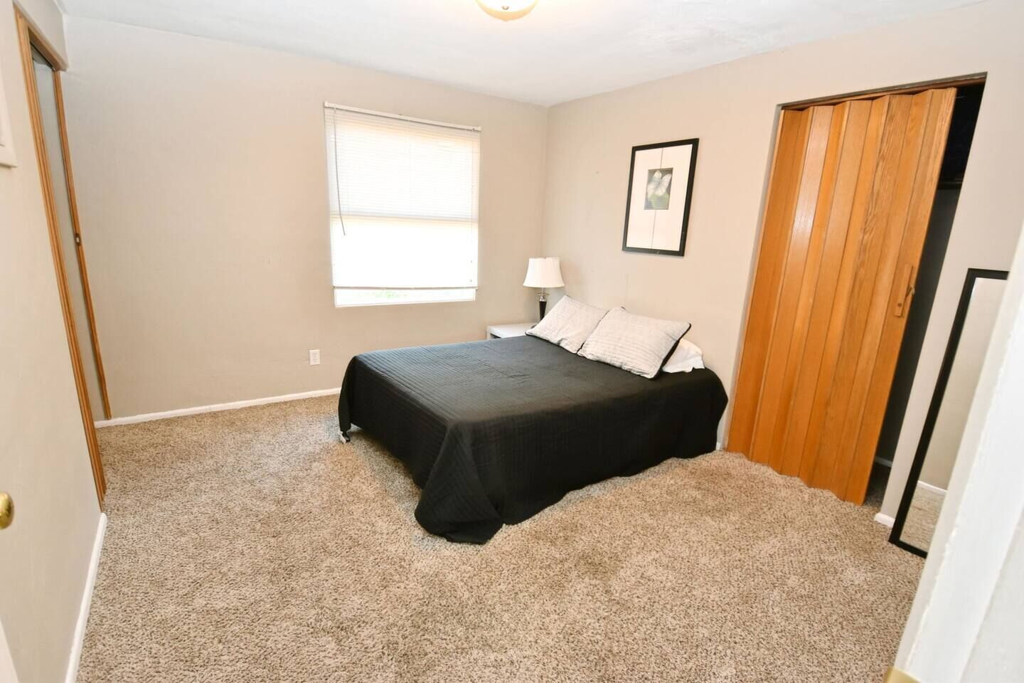 A bedroom with a bed, a window, a nightstand, a lamp, and a door.