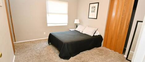 A bedroom with a bed, a window, a nightstand, a lamp, and a door.