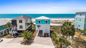 Una propiedad frente a la playa con una casa de dos pisos, un garaje y un camino de entrada que conduce a la playa.