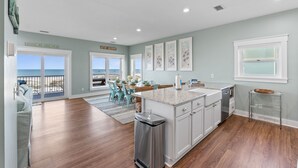 Una cocina con una isla grande, armarios blancos y vista al océano.