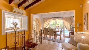 Una habitación amarilla e luminosa con comedor, una escalera y vistas a una piscina.