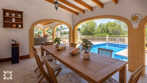 Un comedor con mesa y sillas de madera, vista a una piscina y un balcón con vistas al paisaje circundante.