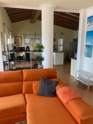 A living room with an orange sofa, a white column, and a kitchen in the background.