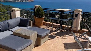 Eine Terrasse mit einer Couch, Stühlen und einem Tisch mit Blick auf die Küste.
