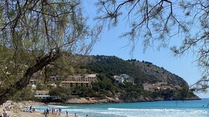 Ein Strand mit Menschen, die spazieren gehen und sitzen, ein klarer Himmel und Gebäude im Hintergrund.