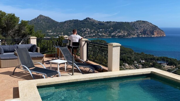 Ein Poolbereich mit Liegestühlen und Blick auf das Meer und die Berge.