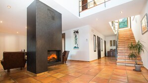 Amplia sala de estar con chimenea, una escalera y un gran ventanal que proporciona luz natural.