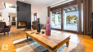 Amplia sala de estar con chimenea, una gran mesa de centro de madera y vistas al exterior a través de puertas correderas de vidrio.