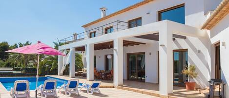 A modern villa with a pool, outdoor seating, and a covered patio area.