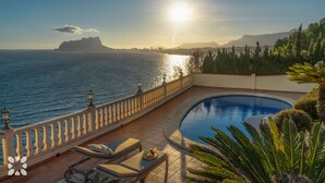 Un espace aménagé au bord de la piscine, offrant une vue sur la mer et les montagnes, une terrasse ensoleillée et des chaises longues.