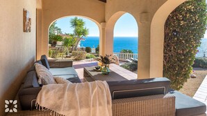 Un espace extérieur aménagé, abrité et doté d’une vue sur la mer, comprenant un canapé, une table avec des boissons et une plante décorative.