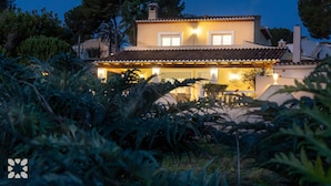 Une maison à deux étages, avec un toit recouvert de tuiles et une véranda bien éclairée à l’avant.