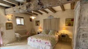 A bedroom with a bed, two bedside tables with lamps, a chair, a mirror, and a rustic ceiling beam. - Cottage in the countryside with pool near the Marais Poitevin (Xaintray)