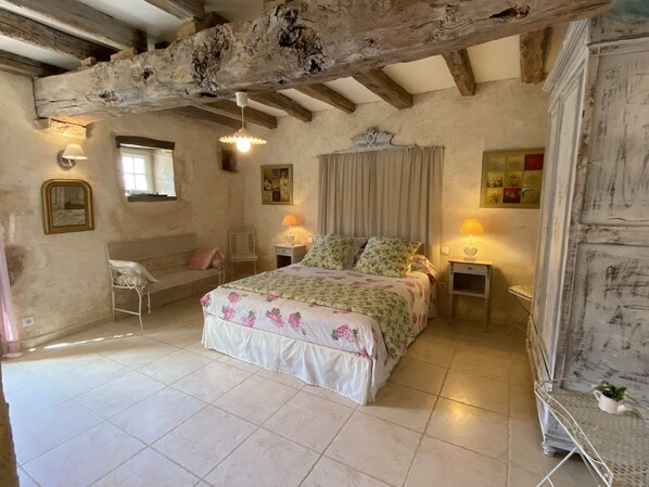 A bedroom with a bed, two bedside tables with lamps, a chair, a mirror, and a rustic ceiling beam. - Cottage in the countryside with pool near the Marais Poitevin (Xaintray)