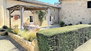 A stone building with a covered patio area, a small garden, and a hedge. - Cottage in the countryside with pool near the Marais Poitevin (Xaintray)