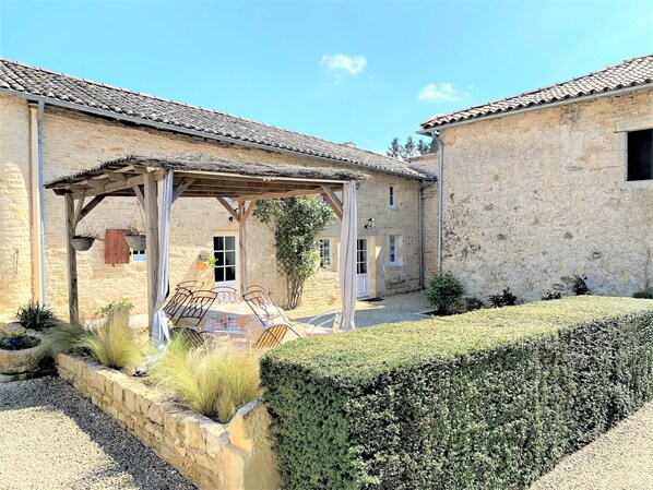A stone building with a covered patio area, a small garden, and a hedge. - Cottage in the countryside with pool near the Marais Poitevin (Xaintray)