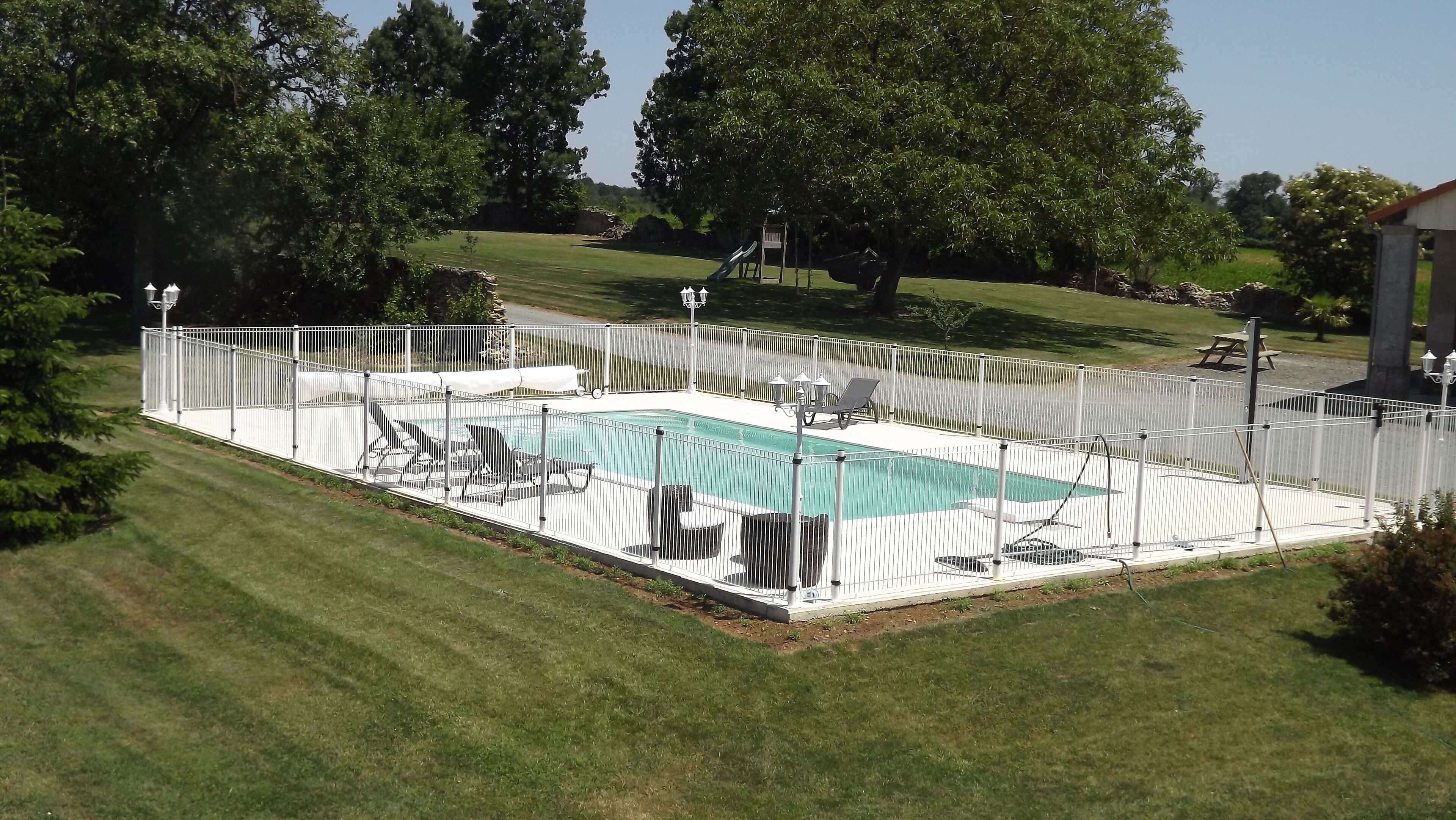 A rectangular swimming pool surrounded by a white fence, with lounge chairs and a small deck area.