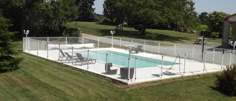 A rectangular swimming pool surrounded by a white fence, with lounge chairs and a small deck area.