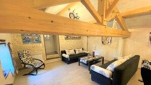 A spacious loft-style living area with exposed wooden beams, a stone wall, and a staircase leading to an upper level. - Cottage in the countryside with pool near the Marais Poitevin (Xaintray)