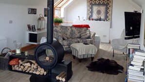 Ein gemütliches Loftsessel-Wohnzimmer mit einem schwarzen Holzofen, einer Couch, einem Couchtisch und einem Bücherregal.