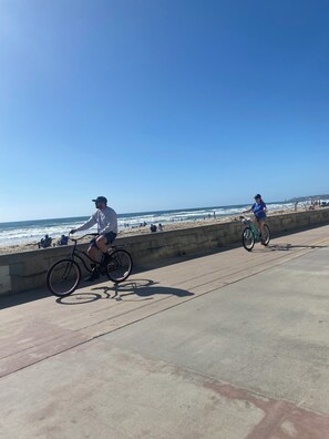 Un chemin en béton qui longe la plage, sur lequel se trouvent deux cyclistes.
