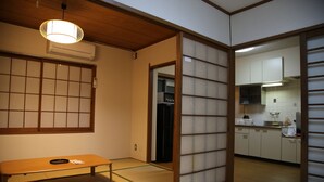 Een traditionele Japanse kamer met tatami vloerbedekking, een futon bed, een lage houten bank en een schuifdeur van shoji-papier die leidt naar een keukenhoek.