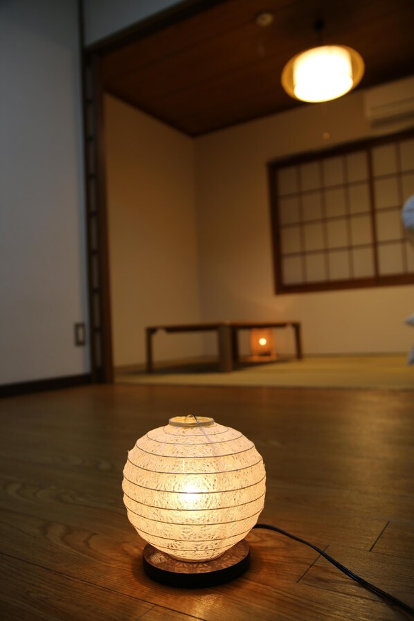 A traditional Japanese paper lantern on a wooden floor, with a wooden table and a window in the background.