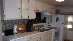Cocina compacta con armarios blancos, microondas, estufa y pileta.