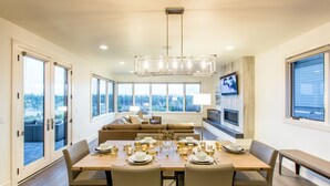 A dining area with a large table set for six, a sofa, and a television in the background. - SPACIOUS ~ 24-hr staff ~ clean + modern ~ wifi ~ parking ~ hot tub ~ firepit 🐶 (Bend)
