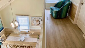 A wooden dining table with chairs, a hanging light fixture, a blue armchair, and a window with blinds. - Oceanfront Luxury House with Stunning Views (Emerald Isle)
