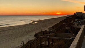 A beach view with a sunset, wooden boardwalks, and buildings in the background. - Oceanfront Luxury House with Stunning Views (Emerald Isle)