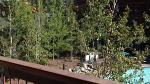 Une vue d’une piscine entourée d’arbres et de bâtiments, avec une chaîne de montagnes en arrière-plan.