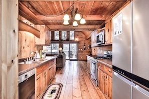 Interior de una cabaña de madera con cocina, que incluye un refrigerador, estufa y alacenas.