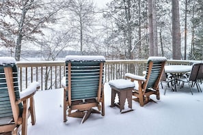 Des chaises et des tables en bois, placées sur une terrasse dotée d’une rambarde et entourées d’arbres, sont recouvertes de neige.