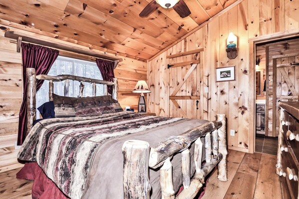 A wooden cabin bedroom with a bed, curtains, a lamp, and a picture on the wall.