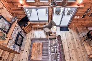 L’intérieur d’un chalet accueillant, avec une cheminée en pierre, un canapé, une table basse et de grandes fenêtres donnant sur un paysage enneigé.