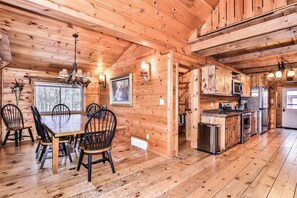 A wooden cabin interior with a dining area, kitchen, and a large window with a view.