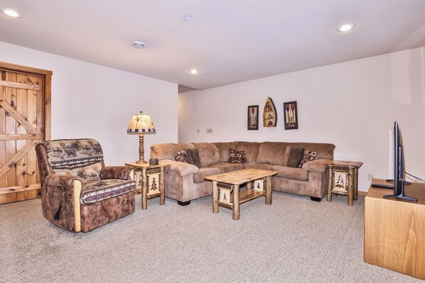 A living room with a sofa, armchair, coffee table, lamp, and a television.