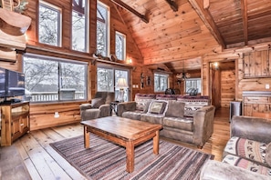 L’intérieur d’un chalet accueillant, avec un plafond en bois, de grandes fenêtres, un canapé, une table basse et un téléviseur.